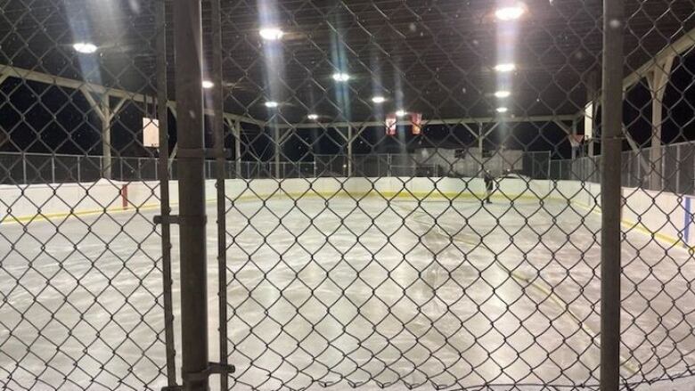 A view through a chain-link fence of a man flooding an outdoor rink 