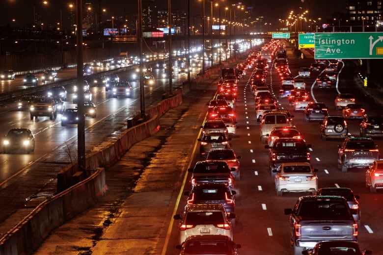 Gridlocked cars on a Toronto highway at night. It is dark and wet.