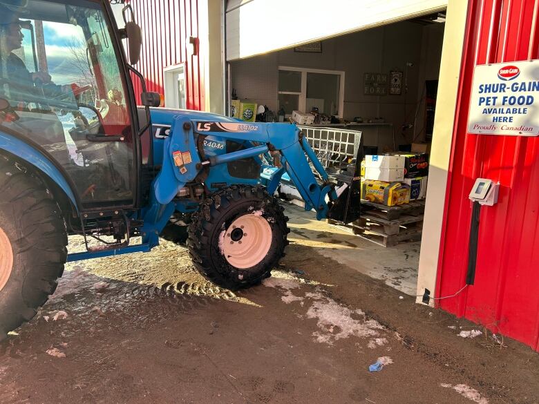 a blue tractor with a pallet on the front moves out of a red building.