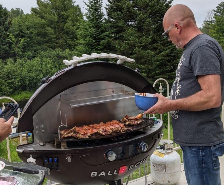 A man cooks food on an open barbecue that's in the shape of a football.