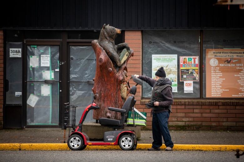 A resident of Hope B.C. stands by his scooter in the town's downtown on Jan. 31. 2024 with a chainsaw carving nearby.