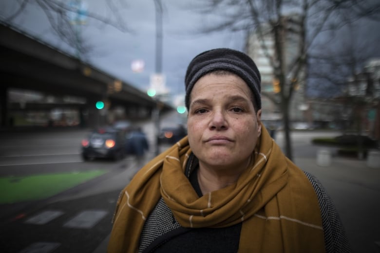 A portrait of a woman with a hat and scarf looking solemn on a city street.