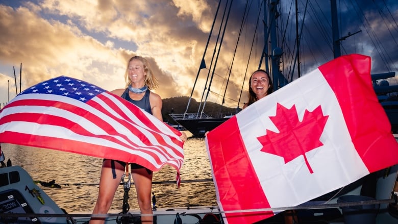 Two women on a boat hold up Canadaian and United States flags.