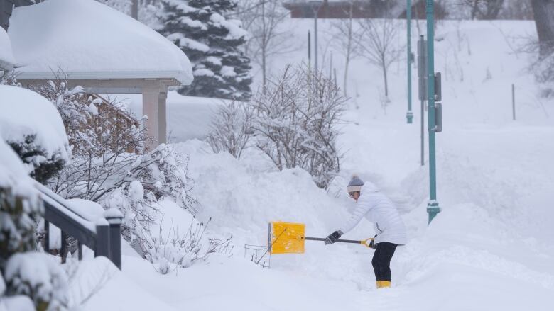 A person wearing a white coat and black pants shovels snow in Halifax on Saturday, Feb. 3, 2024.