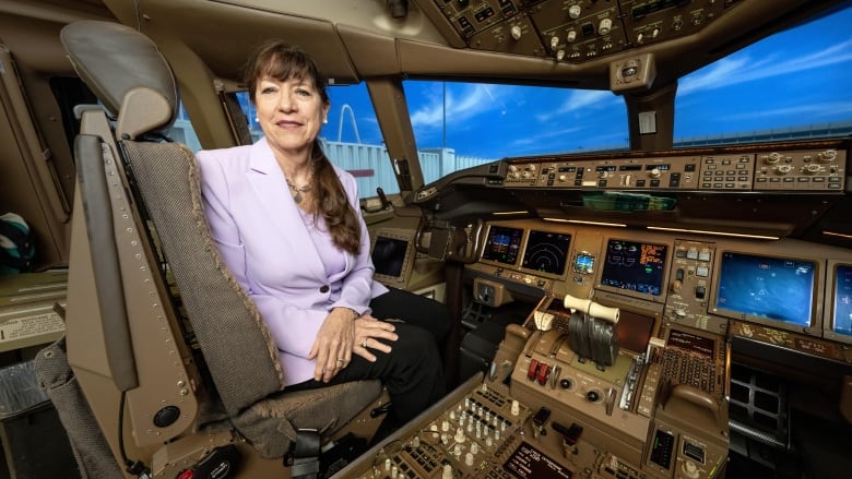 A white woman wearing a pink top sits at the helm of an aircraft.