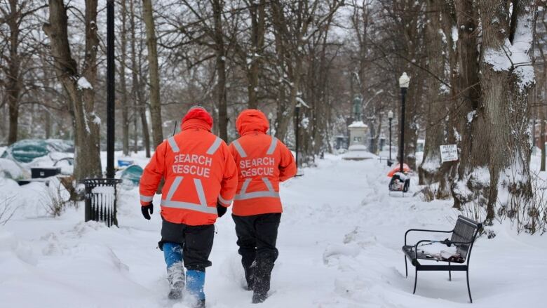 Two people in bright orange search and rescue jackets walk down a snowy path in a city park.