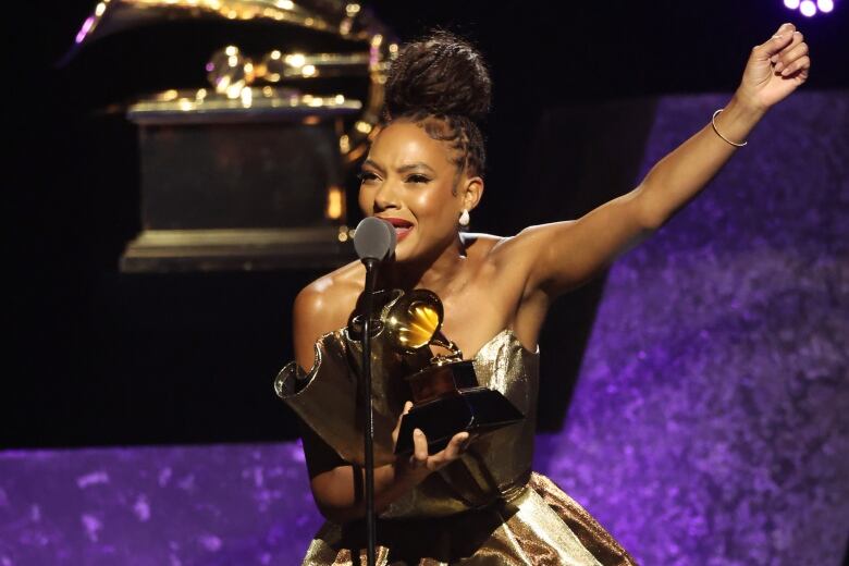 A woman speaks into a microphone while holding an award in one hand and raising the other one upward.