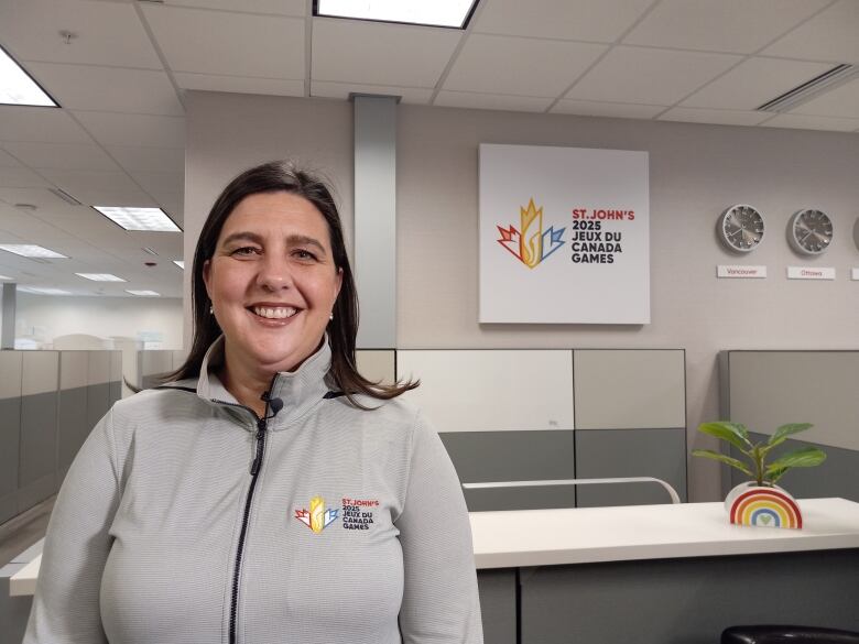 Woman in grey sweater smiling in an office. behind her is sign saying 