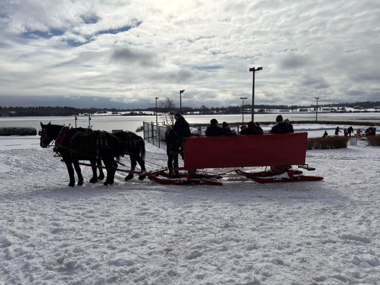 Two horses pulling a red sleigh with a frozen river in the background. 