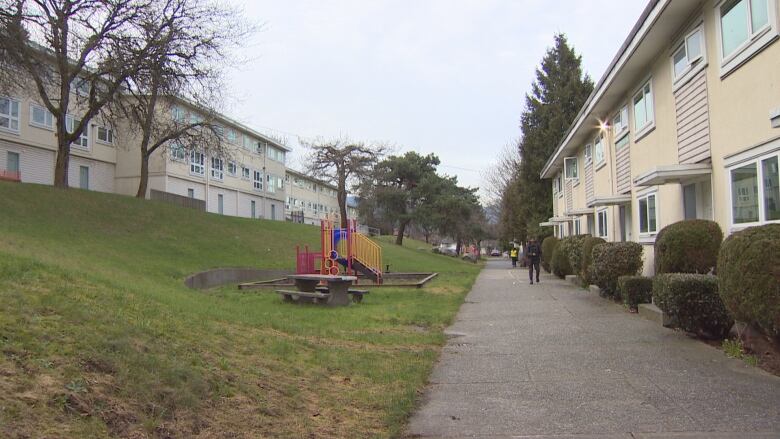 A playground stands between a row of townhomes and an apartment building.