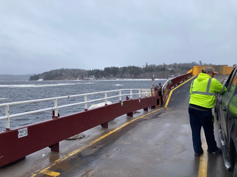 From behind, a man in florescent jacket leans into truck parked on ferry.