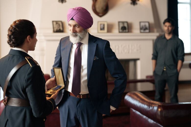 A man in a suit and wearing a turban faces a woman in a police uniform presenting him with a medal. 