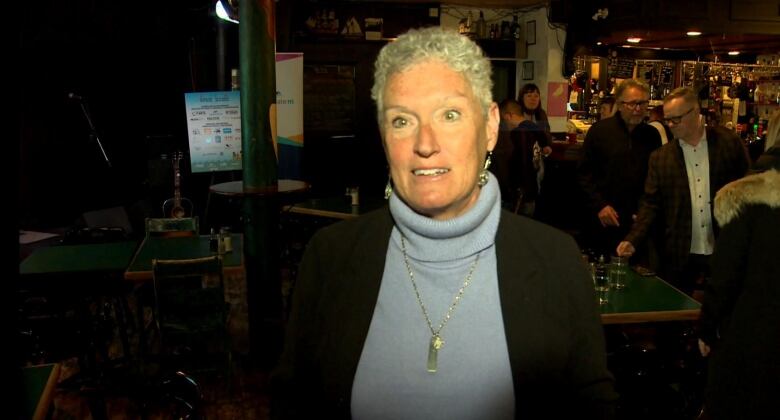 Woman with short hair and light blue turtleneck and black sweater smiling.