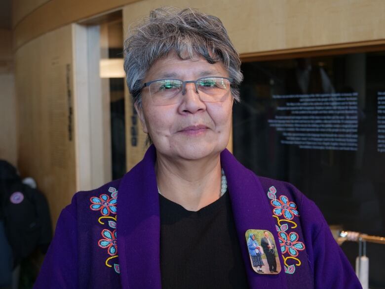 Woman in purple jacket looks at camera.