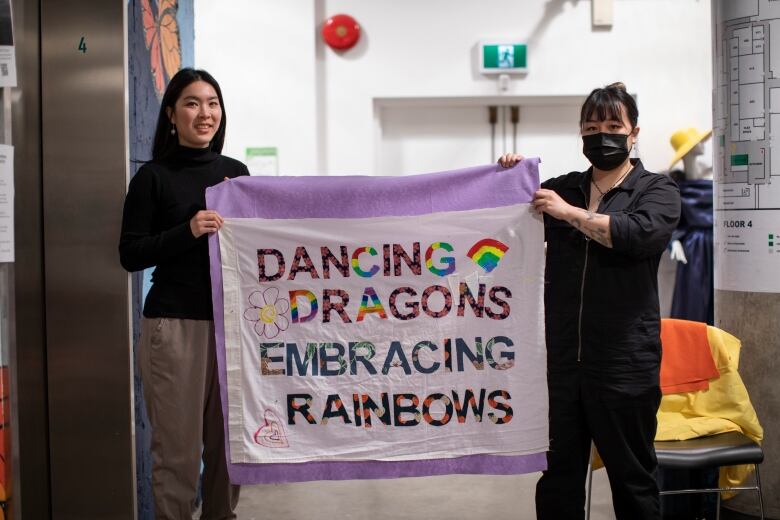 Two women hold a banner that reads: 'Dancing Dragons, Embracing Rainbows.'