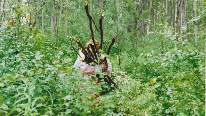 A woman walks through the forest with a bundle of sticks . 