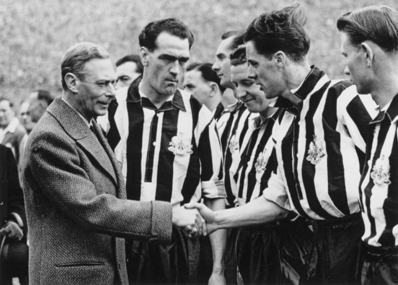 A person shakes hands with an athlete in a uniform standing with teammates.