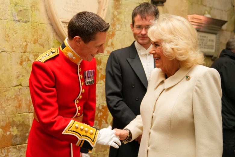 A person wearing a military uniform shakes hands with a person wearing a white coat.