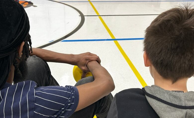 A man and a child sitting on a basketball court.