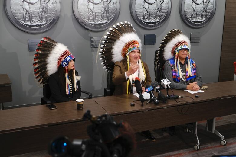 Chief Bobby Cameron sits at a table at a press conference with Second Vice Chief Aly Bear on his left and first Vice Chief David Pratt on his right