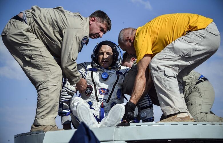 Three men help a Canadinan astronaut get out of a space capsule after his return to Earth.