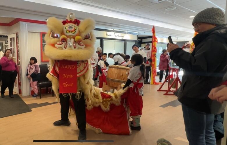 Two people stand in a lion costume, with a Happy New Year banner coming out of its mouth. 