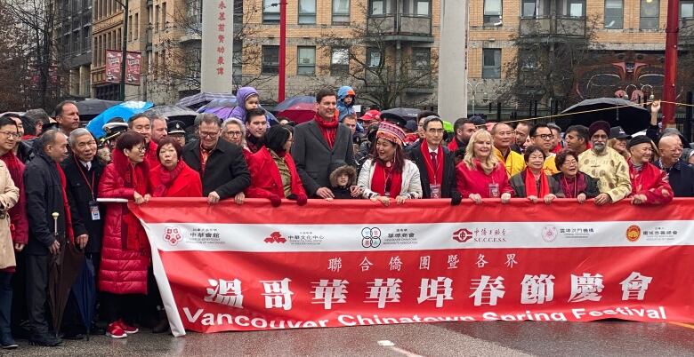 A host of people hold up a red banner in front of a large Chinese gate.