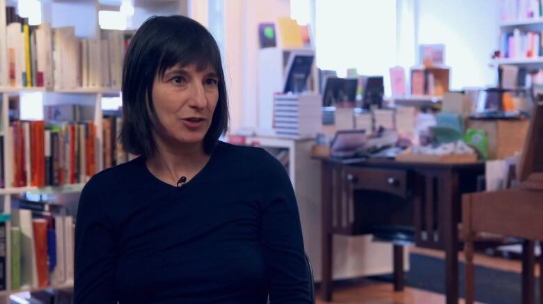 A woman sits in front of a bookshelf.