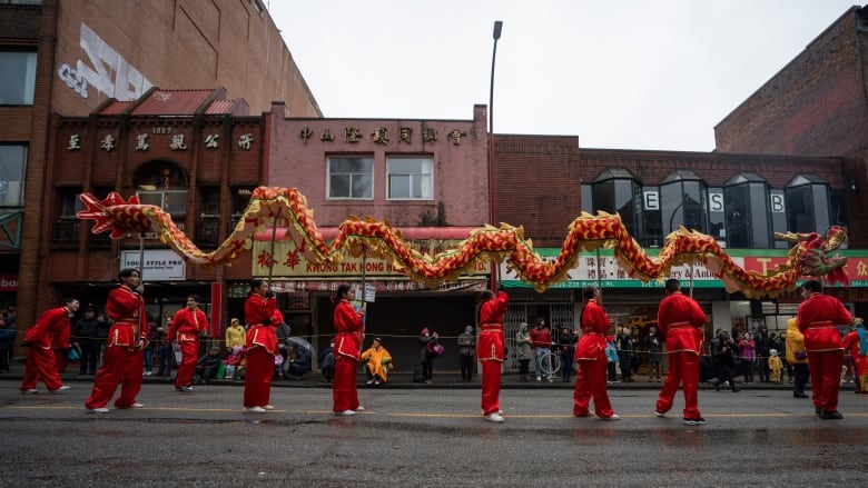 People in traditional Chinese red clothes are holding a long dragon held up by poles. 