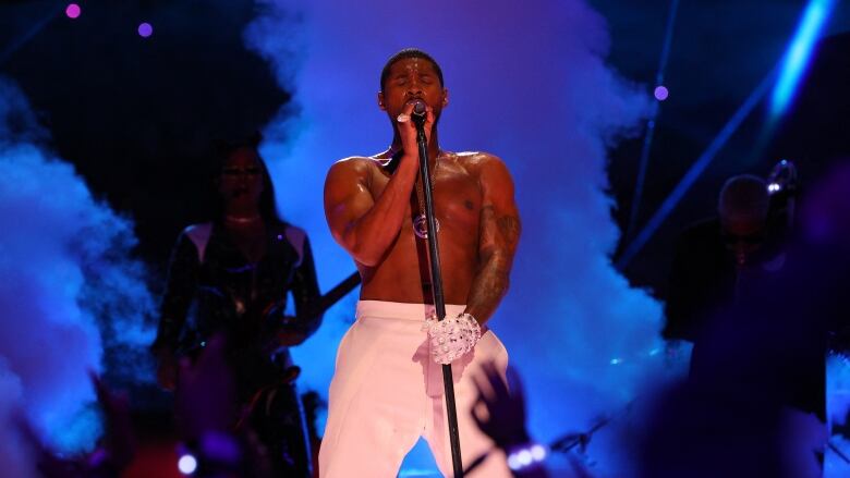 A man  in white pants and a white glove sings into a  microphone on a stage