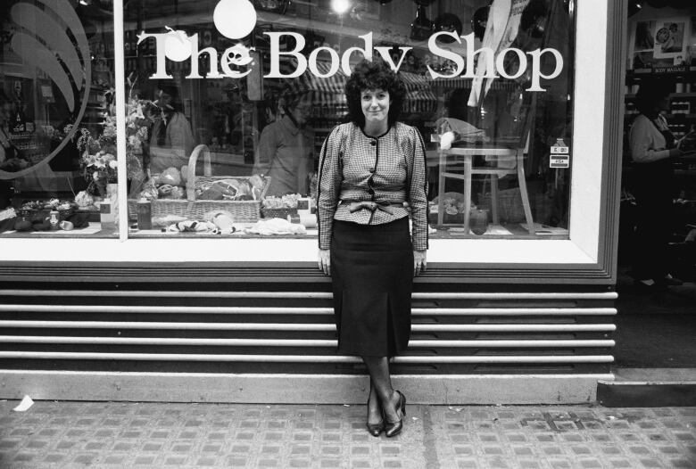 A black and white photo of a woman standing outside a storefront for The Body Shop.