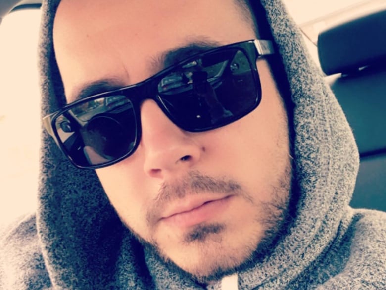 A man wearing sunglasses and a grey hoodie is shown.