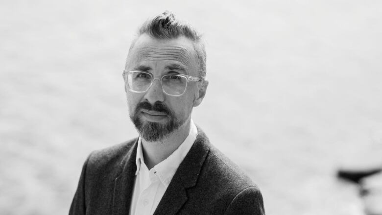 Black and white portrait of a man with short hair, glasses and a goatee wearing a suit.