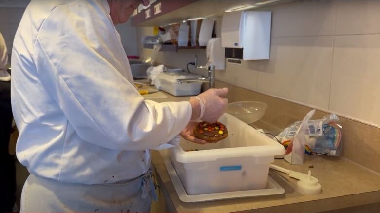 A chocolate maker is stuffing colorful candies into a cookie dough.