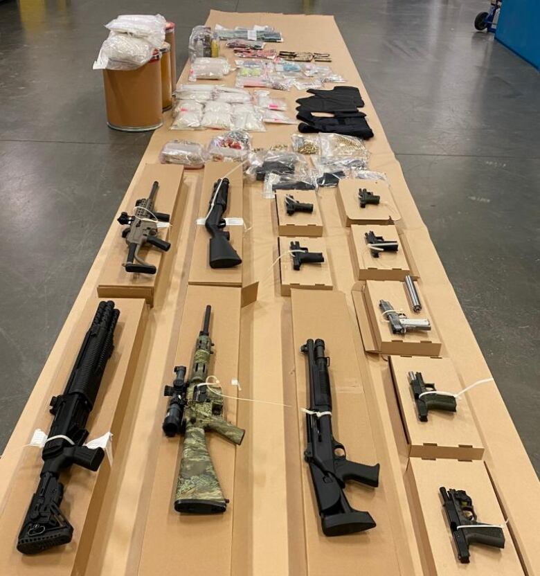 A police seizure displays a number of guns laid out on a wooden display on a floor.