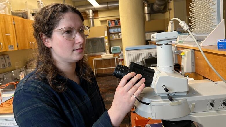 A woman in a blue shirt is shown by a microscope.