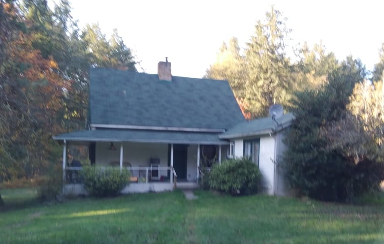 A blurry photo shows a old wood white house with a blue roof in a forested area. 