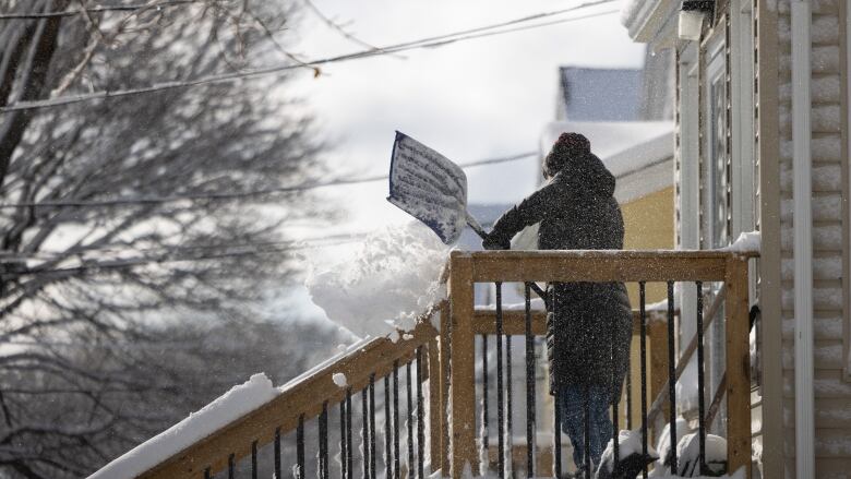 Person at the top of a deck, shoveling snow and throwing it over the side of the deck.