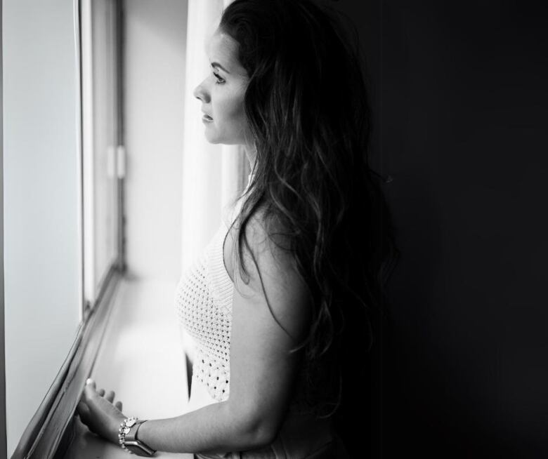 A black and white image of a woman looking out a window.