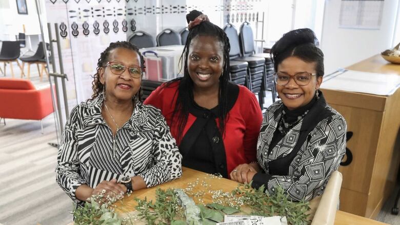 Three Black women stand together and smile at the camera.