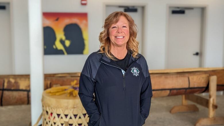 A woman with a Baseball PEI shirt on stands next to Indigenous art