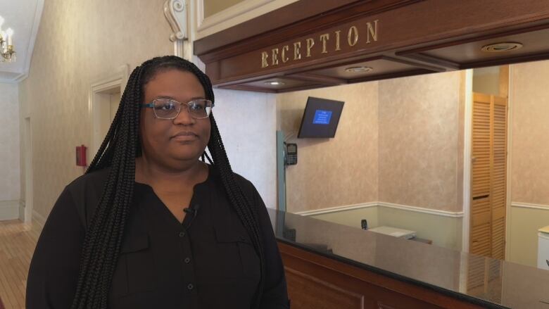 A woman stands in front of an old hotel reception sign doing an on camera interview.