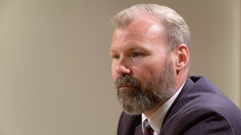 A man with a beard is pictured. He is also wearing a suit.