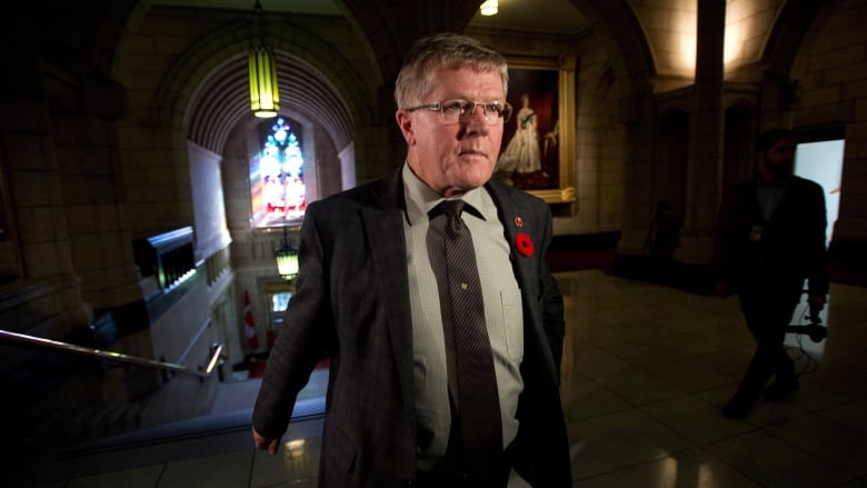 A man in a dark suit walks down a hallway.