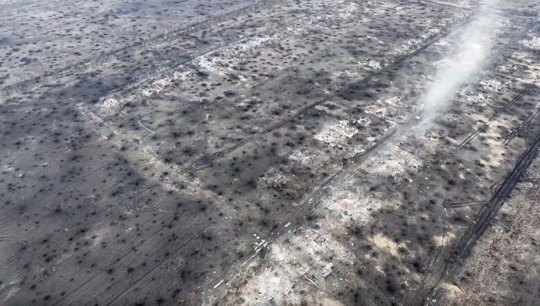 An aerial view shows the ground covered with destroyed buildings and craters from bombardment.