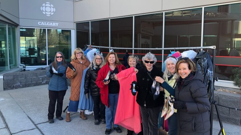 Eight women stand next to a clothing rack.