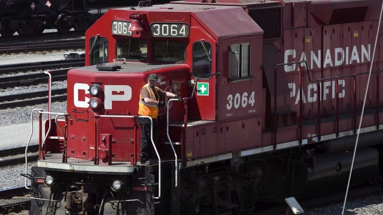 A man in a high-vis vest stands at the front of a train marked 'CP' and 'Canadian Pacific'.