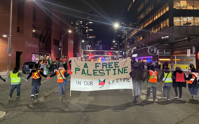 A group of people marching down a road, holding a sign