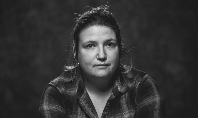 A black and white image shows a woman in a plaid shirt with her dark hair tied back. 