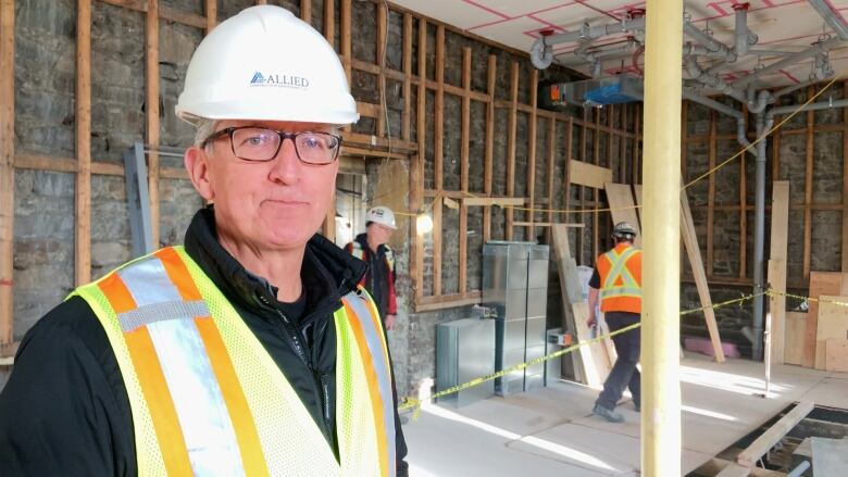 A man wearing a hard hat and vest stands in a room under construction.